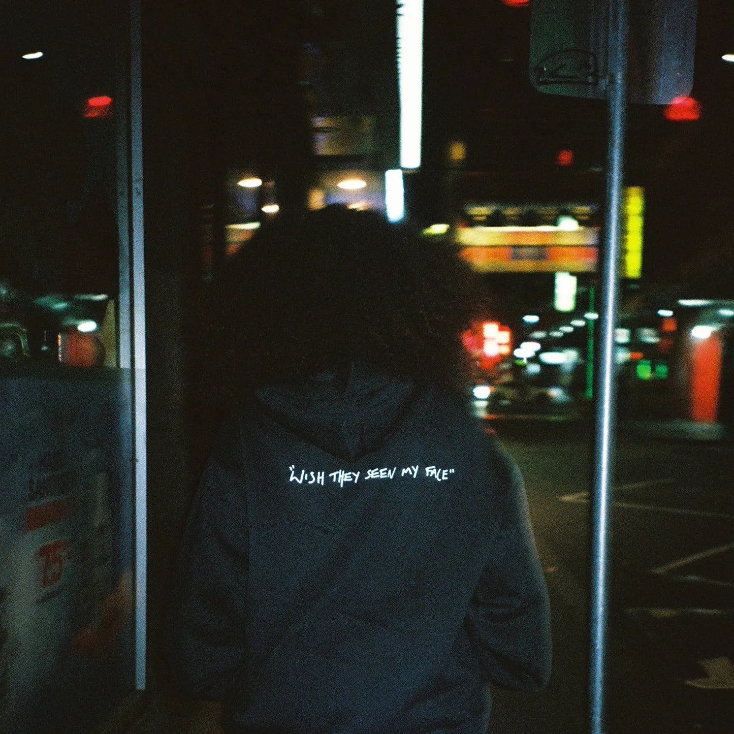 Person wearing the green Lithe hoodie with "wish they seen my face" text on the back, walking down a street at night. Created after the popular single. Released in 2022.